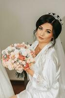 Portrait of a bride in a white robe with a beautiful hairstyle and a bouquet of flowers in her hands, looking at the camera. Sensual cute bride posing. The concept of luxury among fashionable style. photo