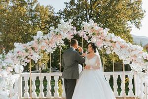 happy bride and groom at the wedding ceremony drinking champagne. The wedding arch is decorated with rose flowers photo