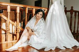 A happy bride is preparing for her luxury wedding in a hotel room, holding her beautiful dress. Portrait of a woman with professional hair and makeup and a smile in a dressing gown photo