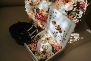 Gold wedding rings in a box decorated with flowers. Black men's belt. Details of the groom photo