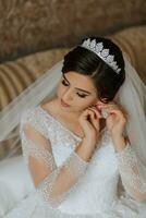 Portrait of a girl in a dressing gown. Happy bride with professional make-up and long veil poses for photographer. The bride puts on earrings and prepares for the wedding photo