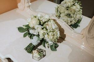 un Boda ramo de flores de blanco rosas cerca un espejo con un reflexión. Boda anillos en un vaso caja foto