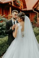 gorgeous elegant luxury bride with veil blowing in the wind and stylish groom kiss on the street near tall autumn trees and wooden houses photo