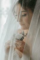 el novia sostiene un flor en el ojal en su manos. Boda flores un lujoso mujer es disfrutando su día. lujo Boda vestido. profesional maquillaje foto