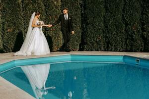 contento Boda Pareja caminando cerca piscina exterior. novia y novio juntos en su Boda día. foto