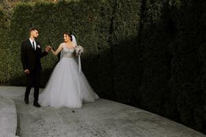 beautiful elegant luxury bride with veil and stylish groom walking on the street near tall autumn trees photo