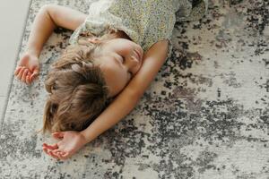 A happy child lies on the background of a modern carpet on the veranda. A little girl rests on the floor of the veranda on a sunny summer day photo