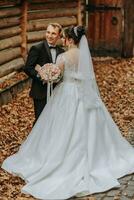 A happy couple of stylish newlyweds in a green park on an autumn day. The bride in a long white dress and the groom in a black suit. Portrait of the bride and groom on their wedding day. photo