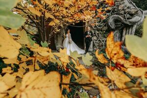 Bride and groom in autumn forest, wedding ceremony, front view. Groom and bride on the background of yellowed autumn leaves. The photo was taken through the yellowing leaves of the trees