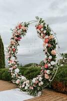 moderno ceremonia en europeo estilo. Boda arco con rosas en el antecedentes de un decorativo jardín. joyería desde Fresco flores, flores y cristales frente vista. foto