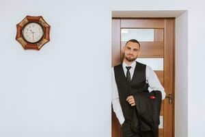 portrait of a man in a white shirt, waistcoat and black tie in a room with natural light. The groom is preparing for the wedding. The man is wearing a white shirt. Stylish groom photo