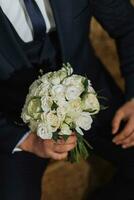 The elegant groom put on a jacket in his room. Details of the wedding morning. Details Beauty and fashion. Groom with a bouquet of flowers close-up photo