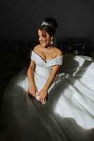 the bride is sitting in a wedding dress by the window under the sun's rays photo