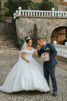 Gorgeous wedding couple walking on stone stairs near old castle in park. Stylish beautiful bride in amazing gown and groom posing on background of ancient building photo