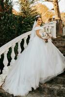 retrato de el novia en el otoño parque en Roca pasos. el novia en un Boda vestir en un natural antecedentes con un ramo de flores de flores en su manos. Boda día. foto