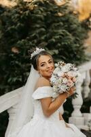 Portrait of the bride in the autumn park on stone steps. The bride in a wedding dress on a natural background with a bouquet of flowers in her hands. Wedding day. photo