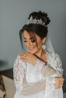 the shy bride covers herself with the sleeves of her lace gown. Portrait of a brunette bride with a tiara on her head and professional make-up photo