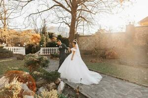 The groom holds the bride's hand and walks. of the bride against the background of the sun's rays, the park and the forest. photo