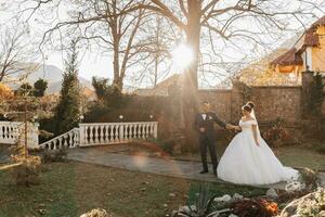 The groom holds the bride's hand and walks. of the bride against the background of the sun's rays, the park and the forest. photo