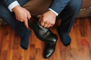 a man in a white shirt, lacing black shoes and preparing to meet his bride. The man wears classic black shoes photo
