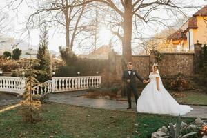 The groom holds the bride's hand and walks. of the bride against the background of the sun's rays, the park and the forest. photo