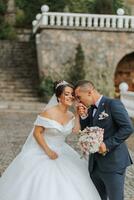 maravilloso Boda Pareja caminando en Roca escalera cerca antiguo castillo en parque. elegante hermosa novia en increíble vestido y novio posando en antecedentes de antiguo edificio foto