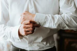 Handsome man putting on shirt standing near window at his room in morning. Preparing for some event or new workday. New opportunities, dating, wedding day or getting ready for job interview concept. photo