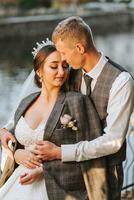 A fabulous romantic newlywed couple is hugging at sunset in an autumn park with leaves from trees on the grass photo