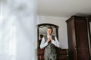 A stylish young man is wearing a suit and tie. Business style. Fashionable image. The groom is preparing for the wedding. Sexy man stands and looks away photo