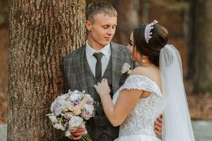 A fabulous romantic newlywed couple is hugging at sunset in an autumn park with leaves from trees on the grass photo