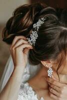 el peluquero hace un de moda y elegante peinado en el de la novia cabello. embellece un peluqueria con un hermosa precioso accesorio hecho de blanco rosario foto