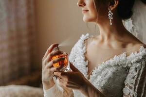 Female beauty. Cute woman at home. The bride sprays perfume on her body. A stylish woman wears a white dress. Spray delicate perfume. Stylish glass bottle of perfume in hands. photo