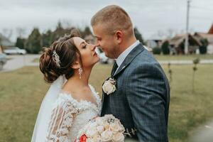 Stylish bride and groom tenderly embrace and kiss. Beautiful bride with modern bouquet embracing stylish groom in autumn park. Sensual romantic moment. Wedding. Stylish and beautiful. photo