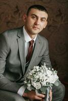 The elegant groom put on a jacket in his room. Details of the wedding morning. Details Beauty and fashion. Groom with a bouquet of flowers photo