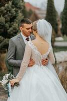 Stylish bride and groom tenderly embrace and kiss. Beautiful bride with modern bouquet embracing stylish groom in autumn park. Sensual romantic moment. Wedding. Stylish and beautiful. photo