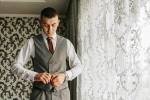 A stylish young man is wearing a suit and tie. Business style. Fashionable image. The groom is preparing for the wedding. Sexy man stands and looks away photo