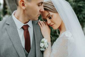 Stylish bride and groom tenderly embrace and kiss. Beautiful bride with modern bouquet embracing stylish groom in autumn park. Sensual romantic moment. Wedding. Stylish and beautiful. photo