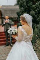 Groom and bride walking and holding hands in the park among tall green trees. Wide-angle autumn photo. Voluminous wedding dress. Classic suit of the groom photo