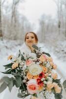 A beautiful bride in a white dress with a bouquet of flowers in the foreground in a fairy-tale snowy winter forest. Portrait of the bride in nature. photo