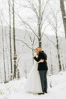 Wedding in winter. The bride and groom are standing against the background of a snowy forest. Walks among rocks and large stones in the forest photo