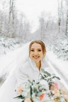 un hermosa novia en un blanco vestir con un ramo de flores de flores en un fabuloso Nevado invierno bosque. retrato de el novia en naturaleza. foto