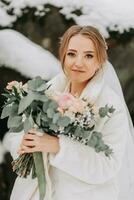 happy bride on the background of snowy rocks with a lush bouquet of flowers in her hands and a blurred background. Portrait of a beautiful bride in a mink fur coat in the cold season photo