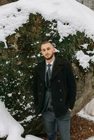 Handsome confident young bearded man standing in snowy yard, fashionable man wearing expensive clothes posing outdoors photo