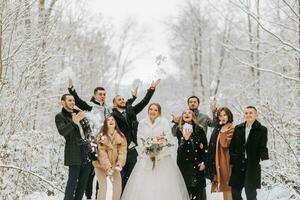 contento recién casados y su amigos en invierno abrigos estar en un cubierto de nieve bosque y lanzar nieve con su manos foto