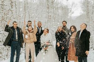 A group of young people, friends of the bride and groom, throw snowballs together with the bride and groom in a fairy-tale snowy forest photo