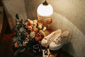 Women's jewelry on a dark background. A gold ring with a diamond on a white background. Necklace, women's wristwatch. Selective focus. White women's sneakers, wedding bouquet photo