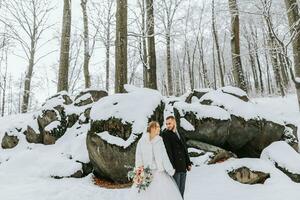 Wedding in winter. The bride and groom are standing against the background of a snowy forest. Walks among rocks and large stones in the forest photo
