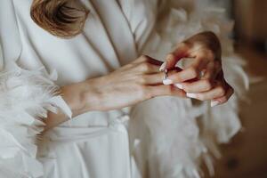 Morning of the bride, woman wearing a white silk robe, close-up photo of female hands. A golden wedding ring on the finger of a young girl close-up