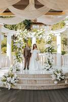 sensitive ceremony of the bride and groom. A happy newlywed couple stands against the background of a wedding arch decorated with fresh flowers photo