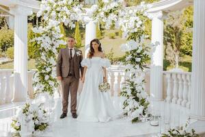 sensitive ceremony of the bride and groom. A happy newlywed couple stands against the background of a wedding arch decorated with fresh flowers photo